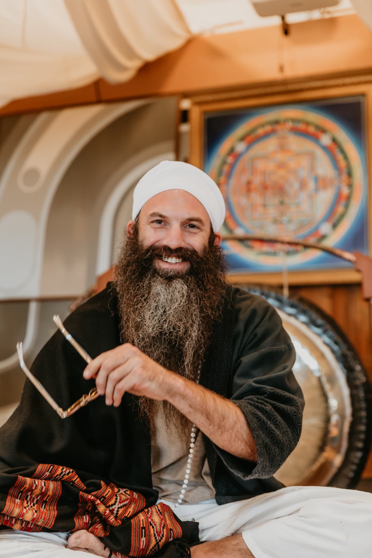 Jai Dev smiling, holding his glasses, seated in the Nevada City studio
